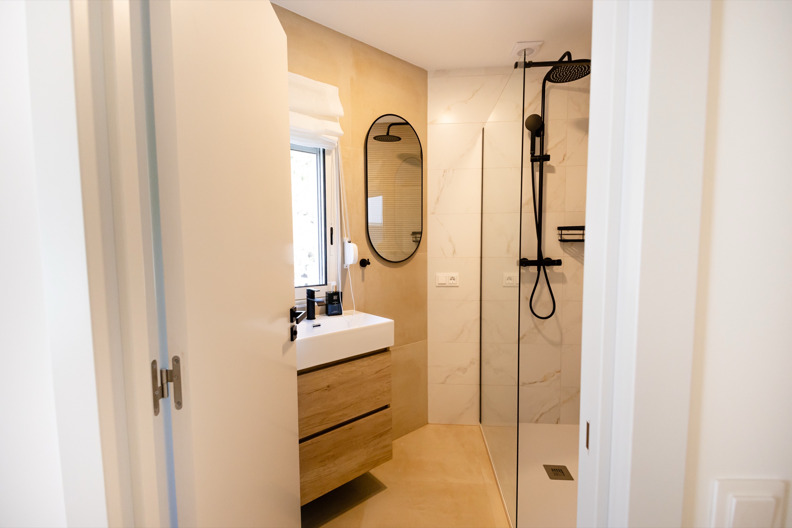Bathroom with oak vanity, oval mirror, and a glass shower with black fittings