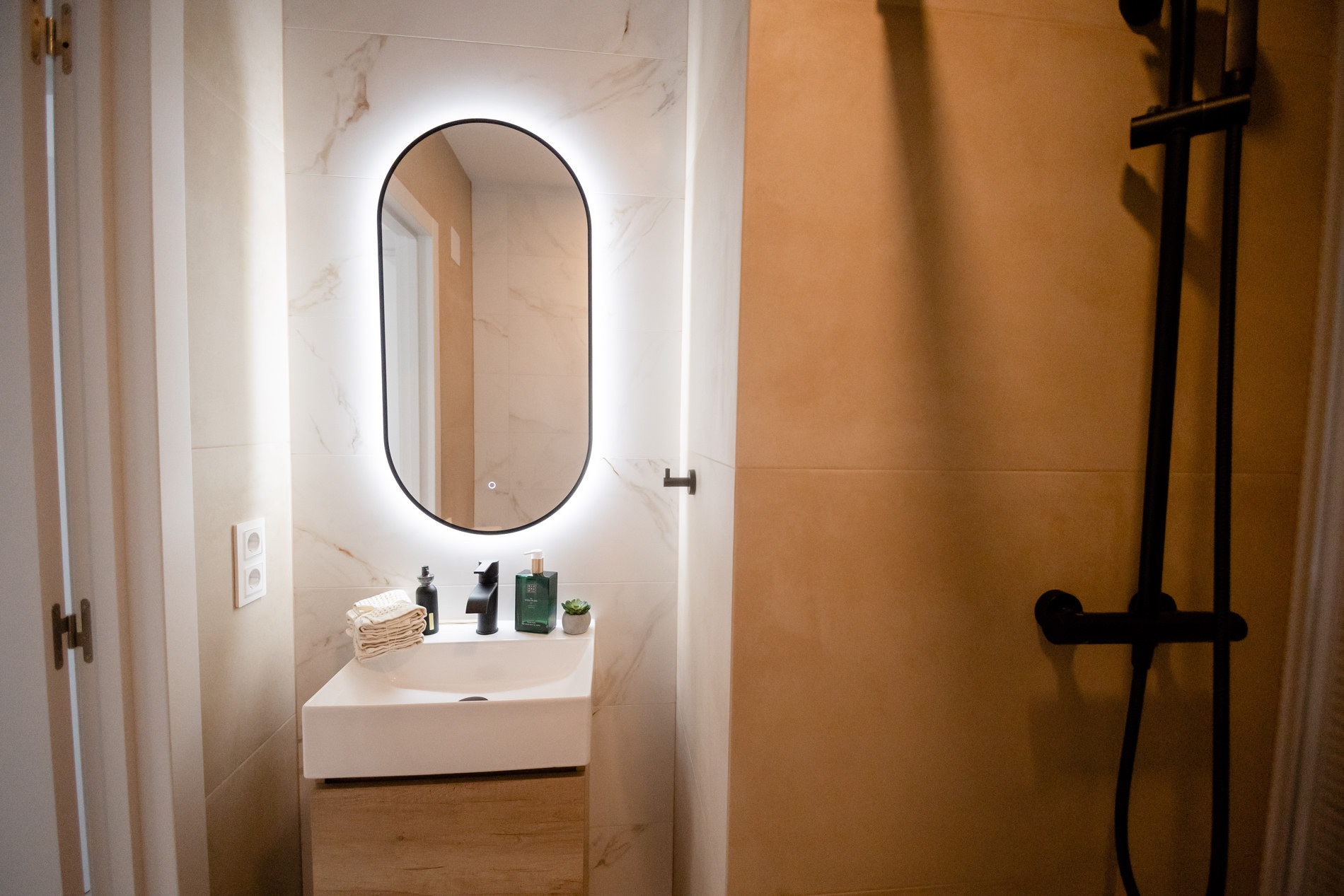 Bathroom with an oval backlit mirror, white basin, and oak cabinet