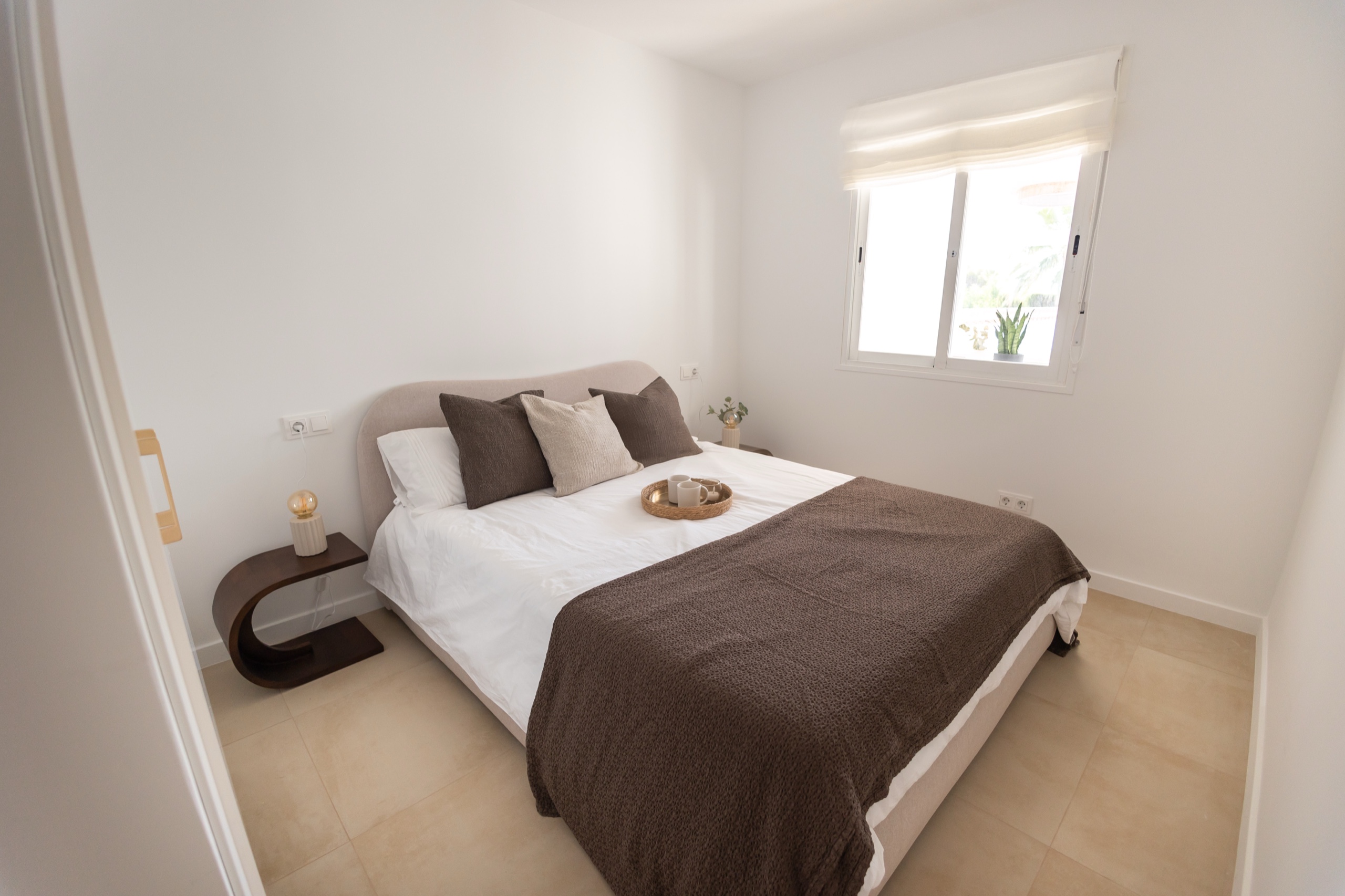 Bedroom with a curved headboard, brown throw, and window to the garden