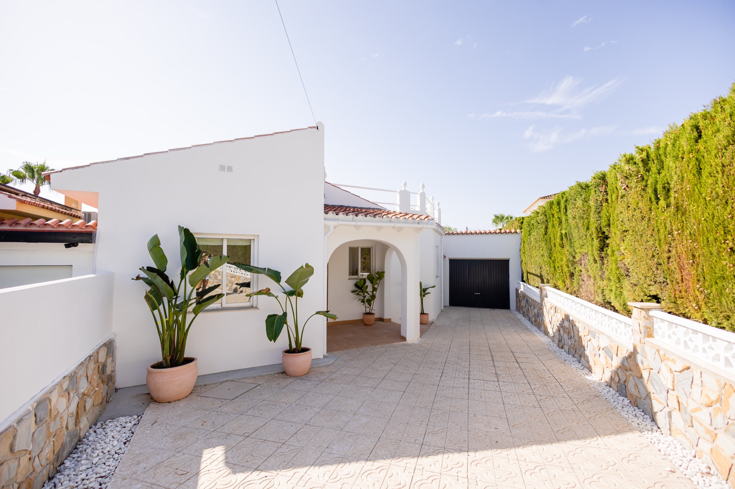 White courtyard with potted plants, an arched porch, and a dark garage door