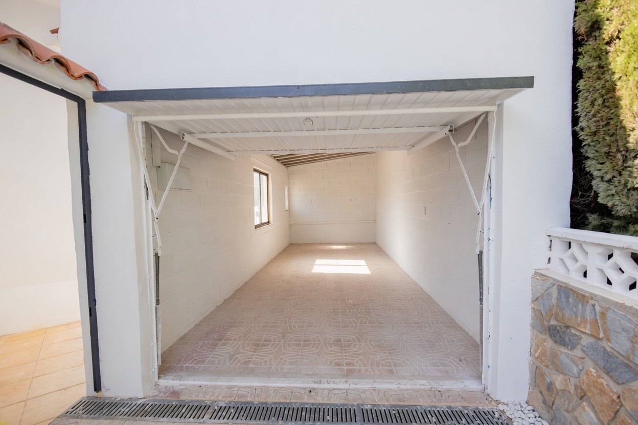 Empty white garage seen from the courtyard, tiled floor in sunlight
