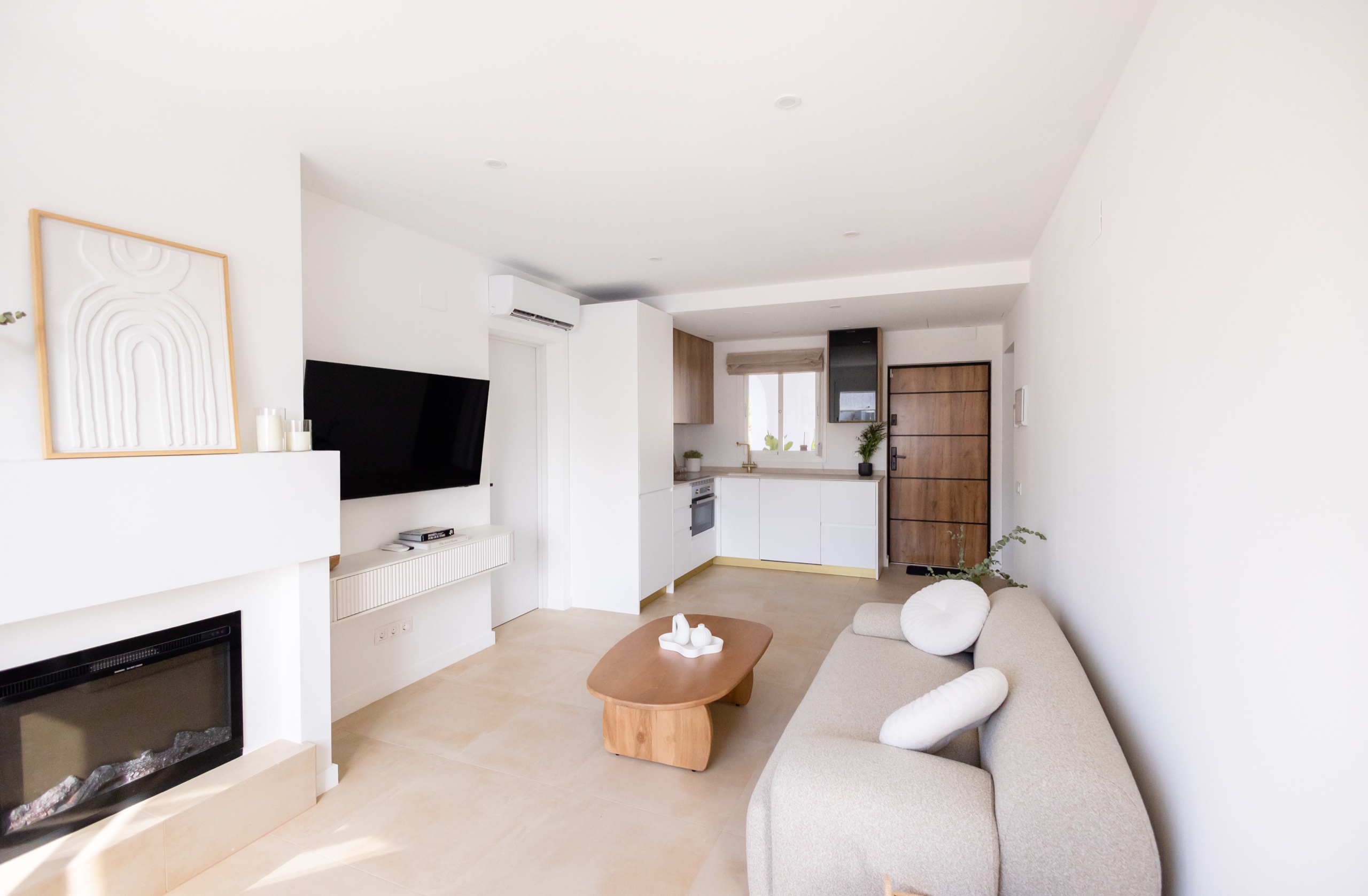 Living room opening to a white kitchen with oak cabinets and a wood front door