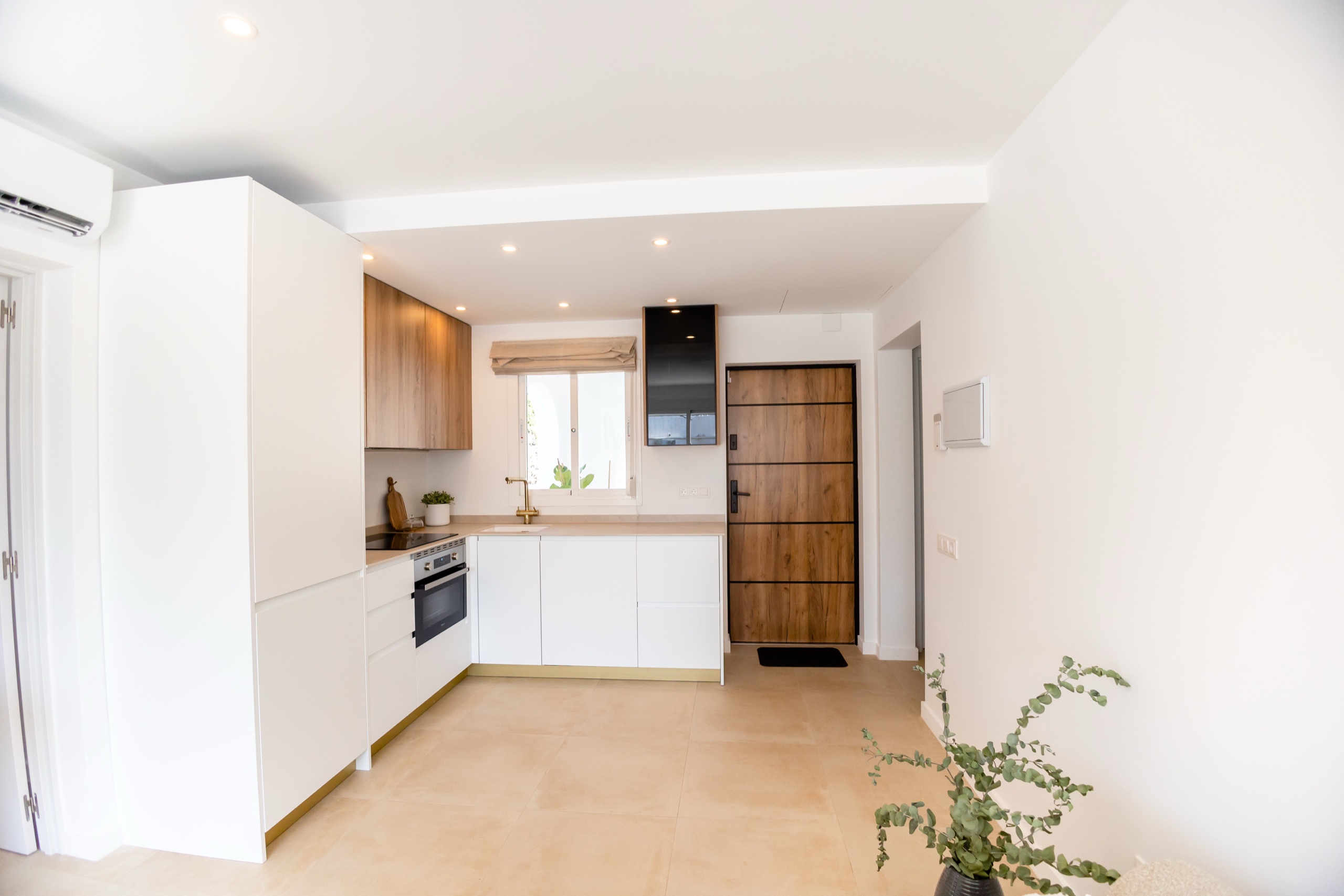 White kitchen with oak uppers, brass tap, and a wood-and-steel door