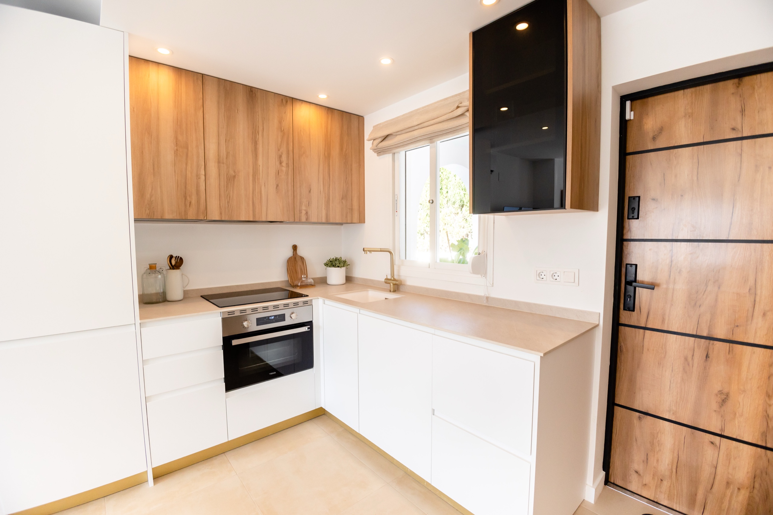 L-shaped kitchen with oak cabinets, stone worktop, and a wood front door